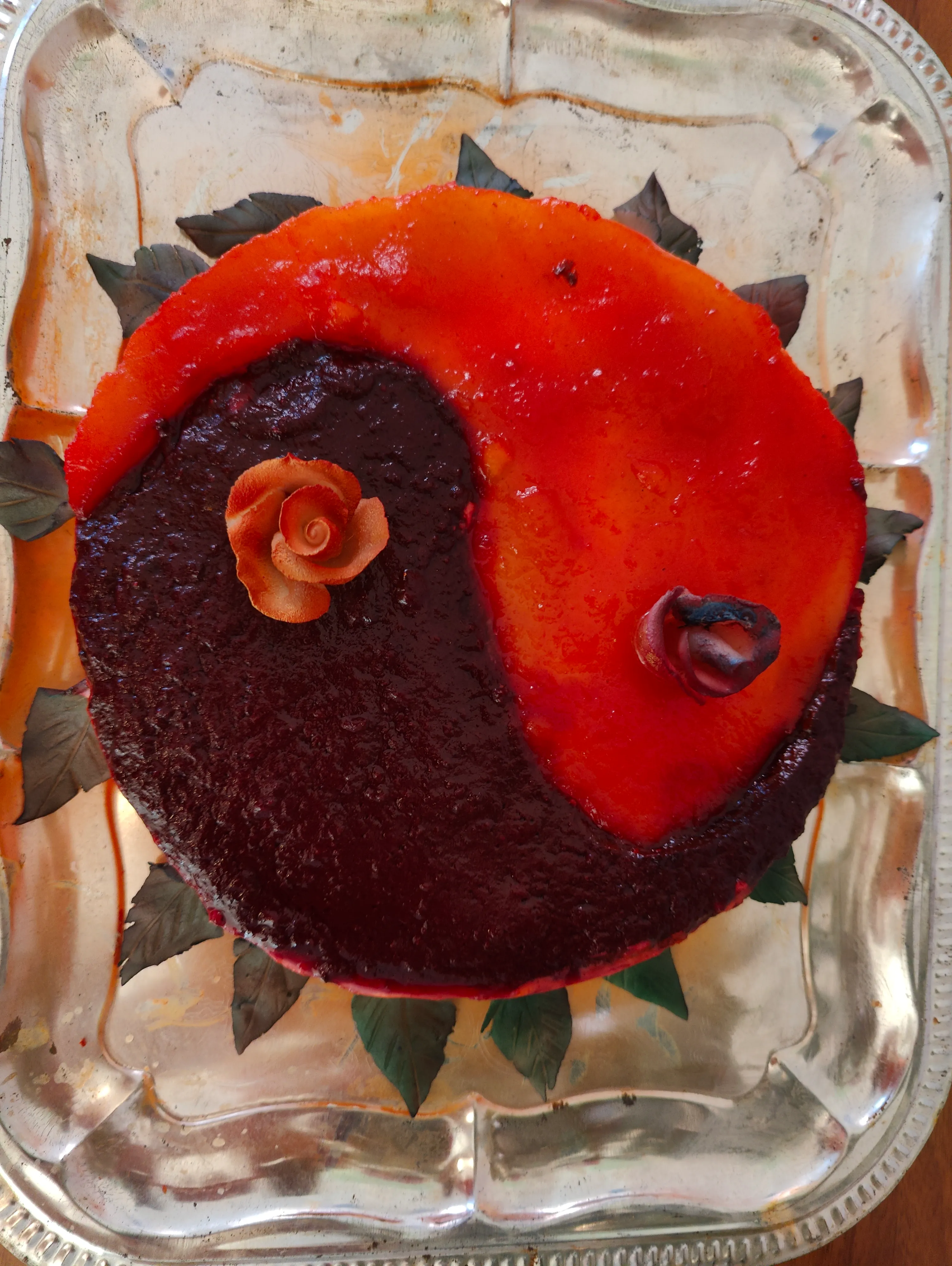 Rund kage set ovenfra, delt i et rødt og et mørkt felt som et yin og yang-tegn, med en lille rose i hvert felt